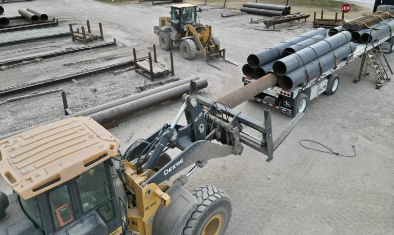 Heavy equipment is used to load telescoping pipe onto a flatbed trailer.