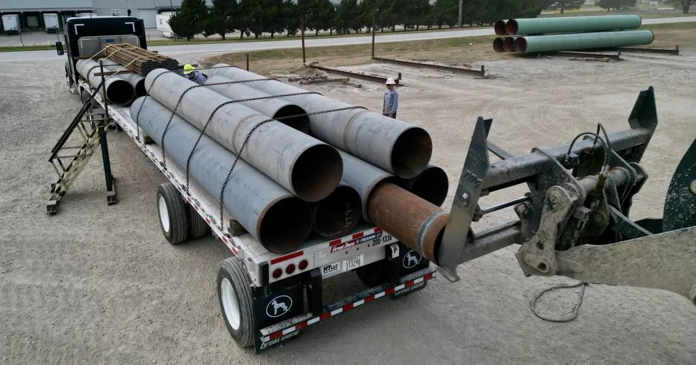 Heavy equipment is used to load telescoping pipe onto a flatbed trailer.